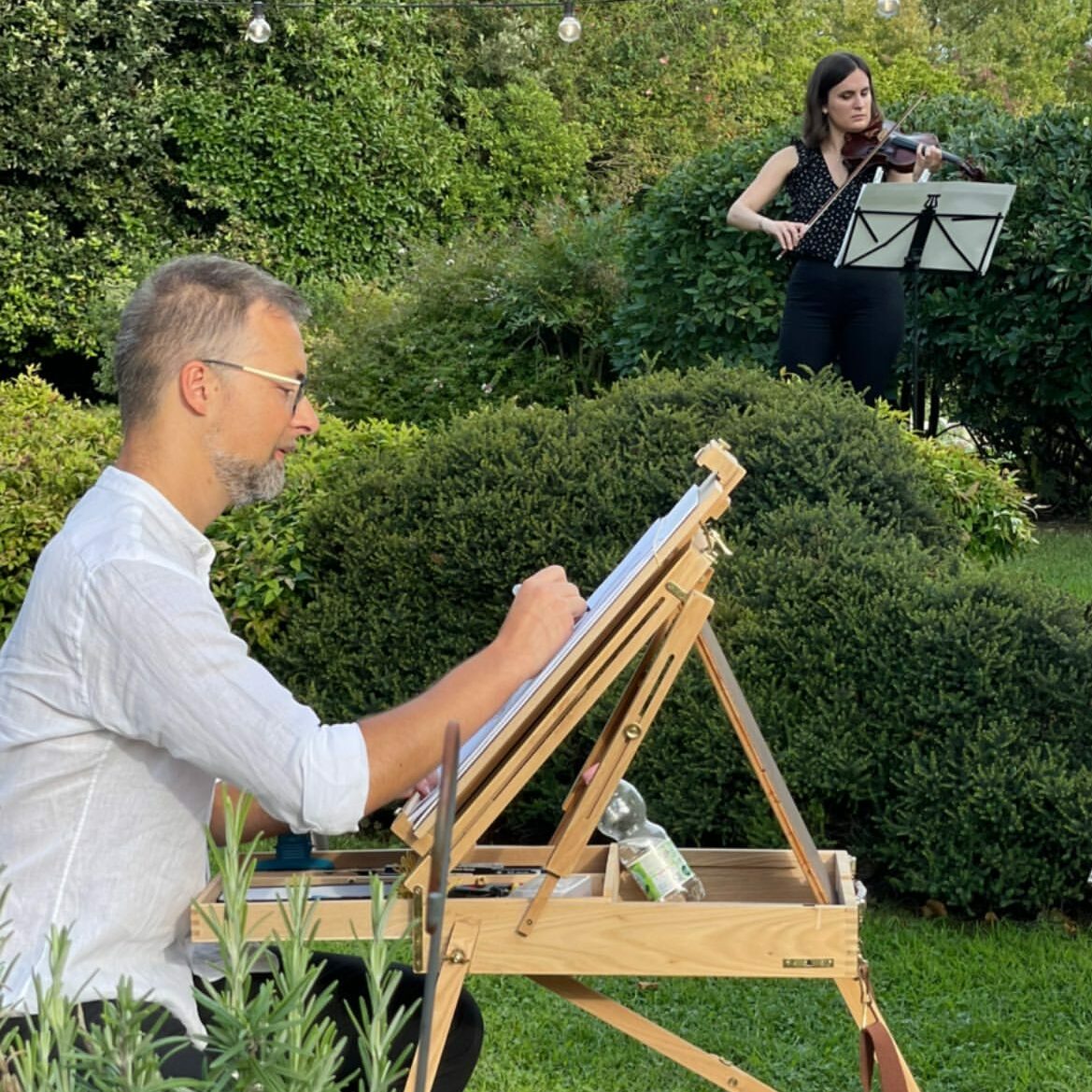Zoom su un caricaturista all'opera durante un matrimonio, sullo sfondo una musicista suona il violino